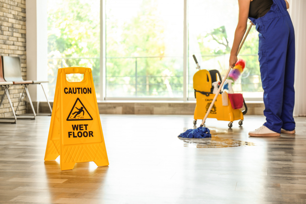 A cleaner mopping a bright commercial lobby beside a wet-floor sign